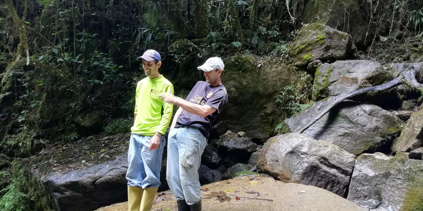 Dos hombres de pie sobre las rocas al pie de la cascada.
