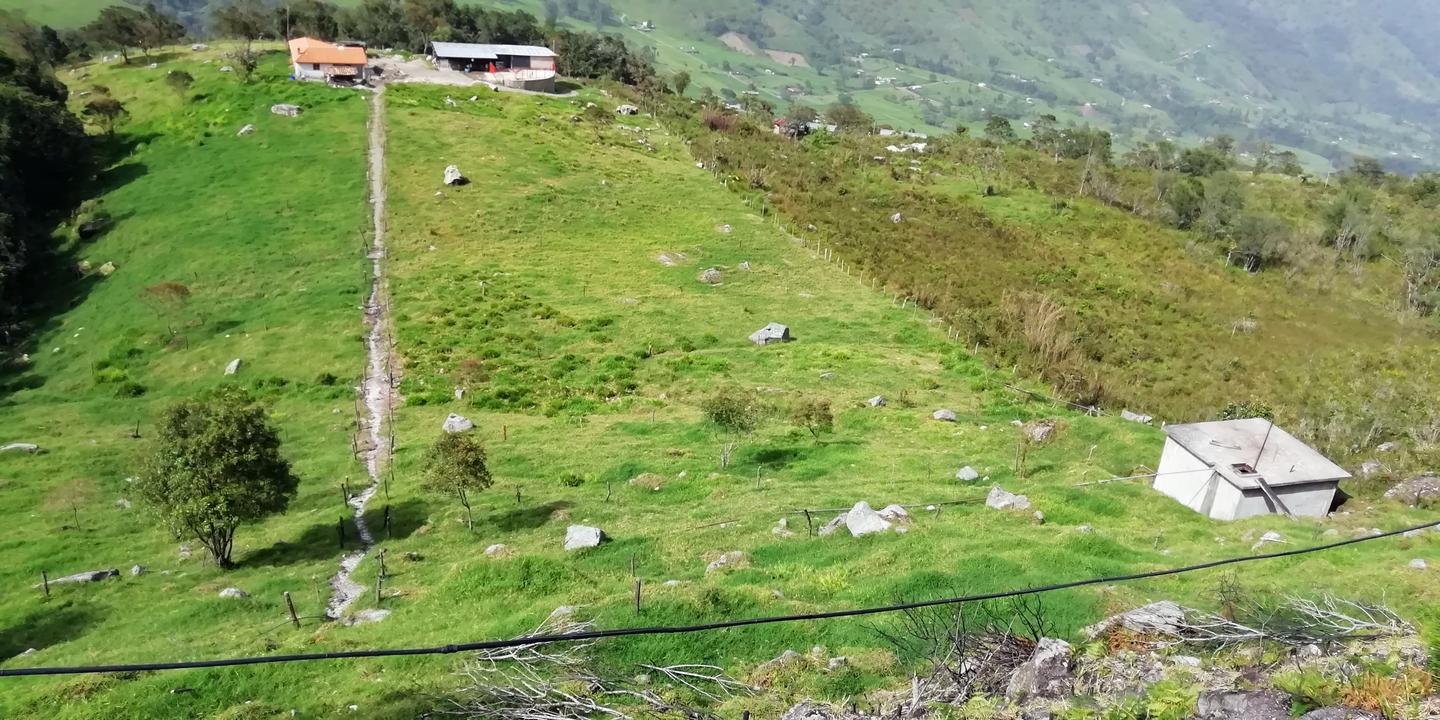 Una loma de pasto verde con una casa arriba y un tanque abajo.