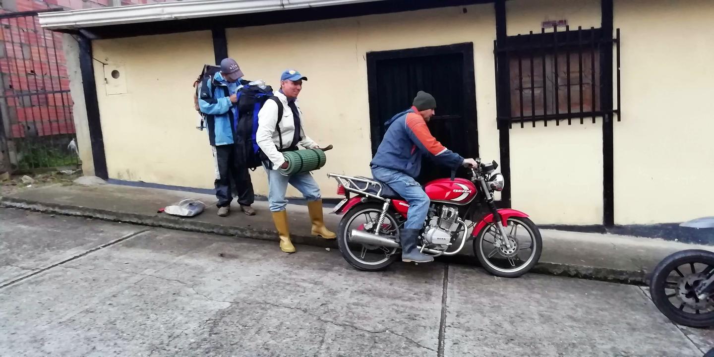 Parte del grupo con morrales frente a una casa; uno en moto.